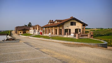 A large building with a driveway, a lawn, and a vineyard in the background.