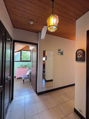 Un pasillo con techo de madera, una lámpara colgante, un aparador rosa y una puerta que da a otra habitación.