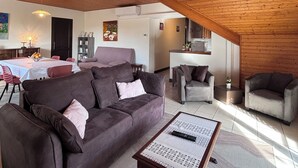 Un vaste espace de vie doté d’un haut plafond en bois, d’un canapé, d’une table basse et d’une cuisine à l’arrière-plan.