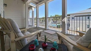 A covered porch with wooden chairs and a table, overlooking a pool and buildings. - Crystal Beach Townhome | Golf Cart & Bikes | Pool View | Walk to Beach & Destin Commons (Destin)