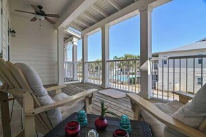 Eine überdachte Veranda mit Holzsesseln und einem Tisch, mit Blick auf ein Schwimmbecken und Gebäude.