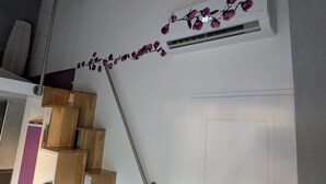 A staircase with a handrail, a white wall, and an air conditioning unit with purple flowers on the wall.