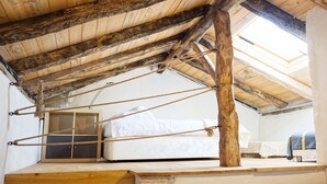 Una habitación rústica con techo de madera inclinado, una cama y un ventanal pequeño.
