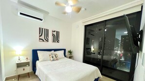 Una camera da letto con un letto, una ventola a soffitto, un comodino con una lampada e una finestra vista sulla città.
