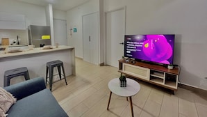 Un soggiorno moderno con una TV a schermo piatto, un divano, un tavolino da caffè e un angolo cottura sullo sfondo.