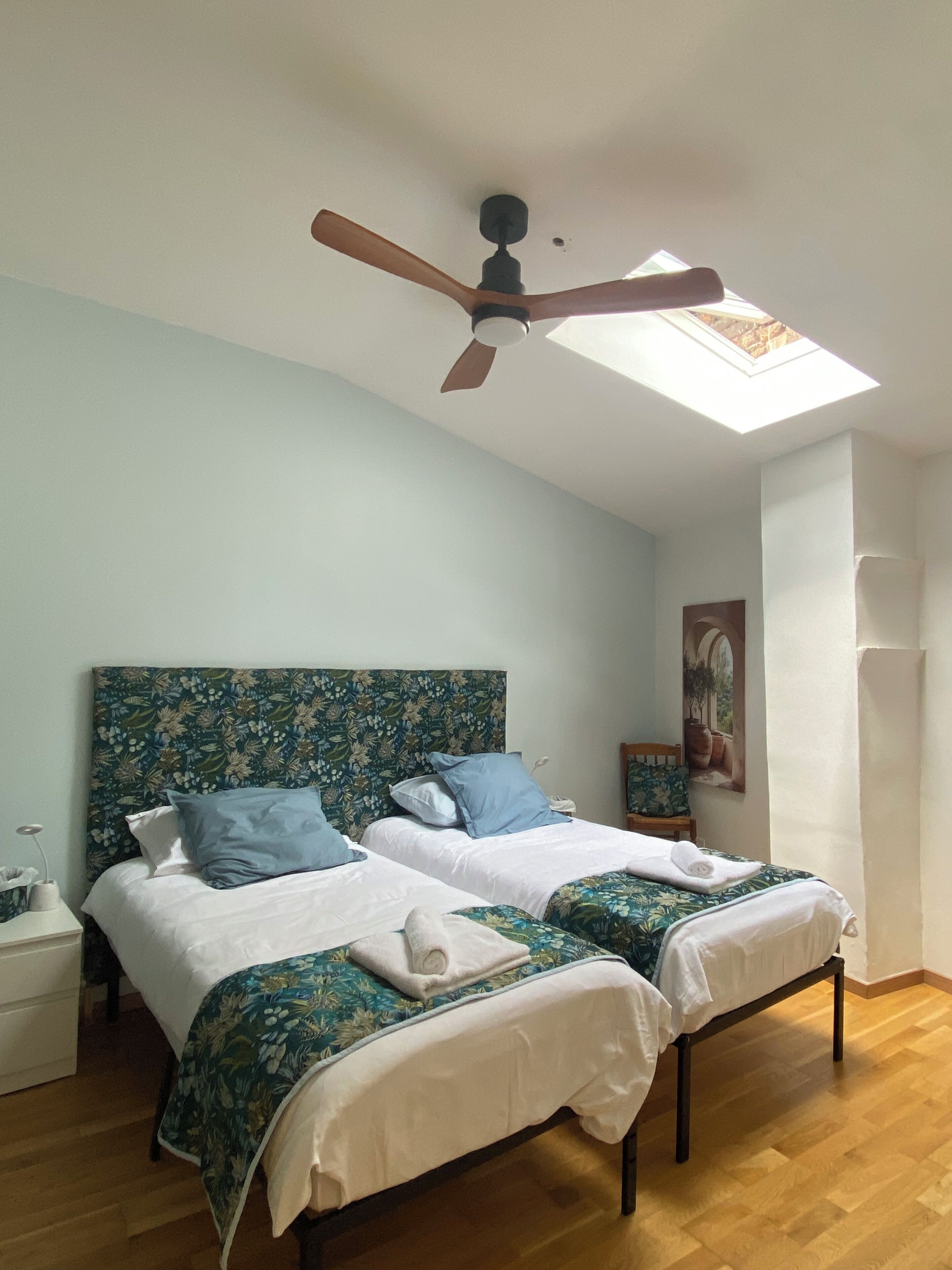 Un dormitorio con dos camas, ventilador de techo, tragaluz y suelo de madera.