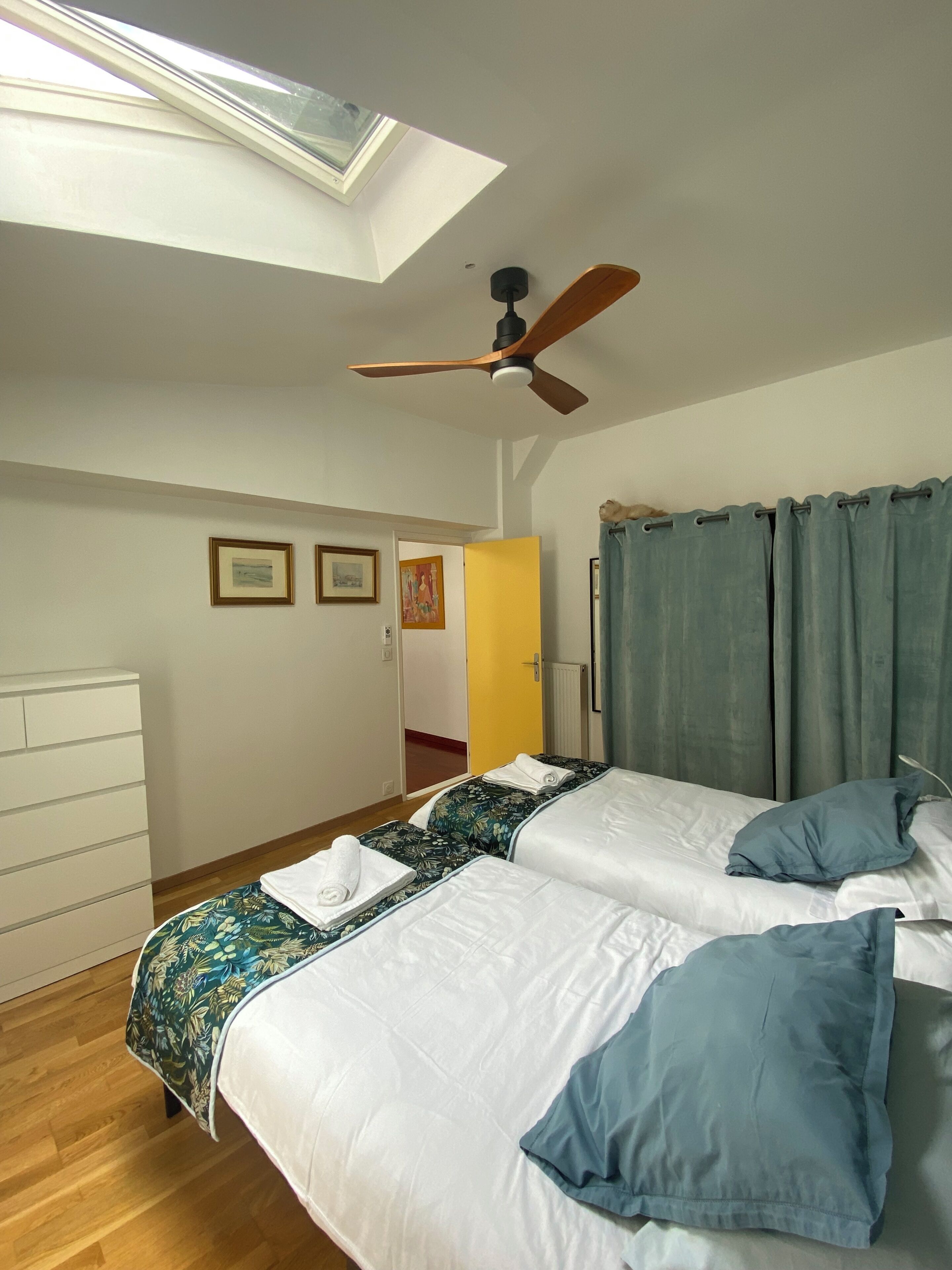 Ein Schlafzimmer mit zwei Betten, einem Deckenventilator, einem Oberlicht, einer Holzkombination und einer Tür zu einem weiteren Raum.