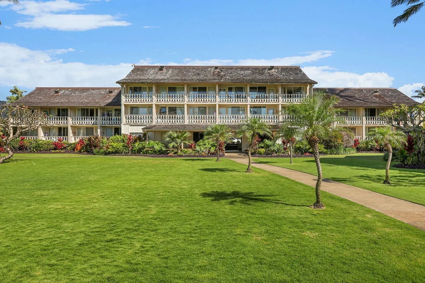 Un hôtel doté d’une grande pelouse, d’un bâtiment à deux étages avec des balcons et d’un aménagement paysager de style tropical.