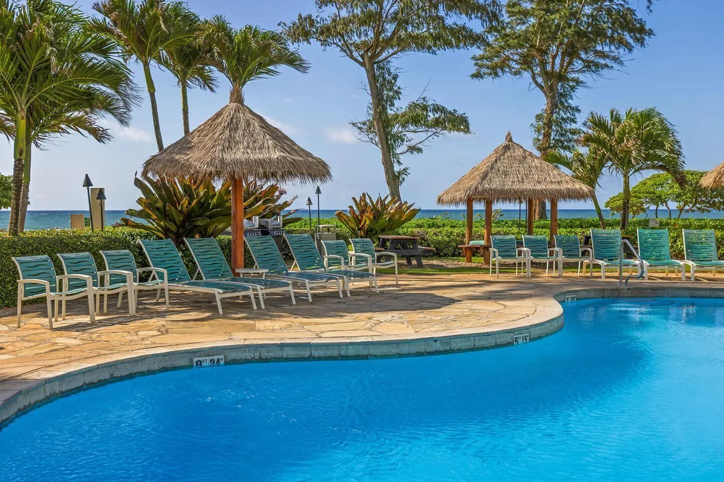 Un espace aménagé au bord de la piscine, avec des chaises longues, des parasols en chaume et une vue sur l’océan.