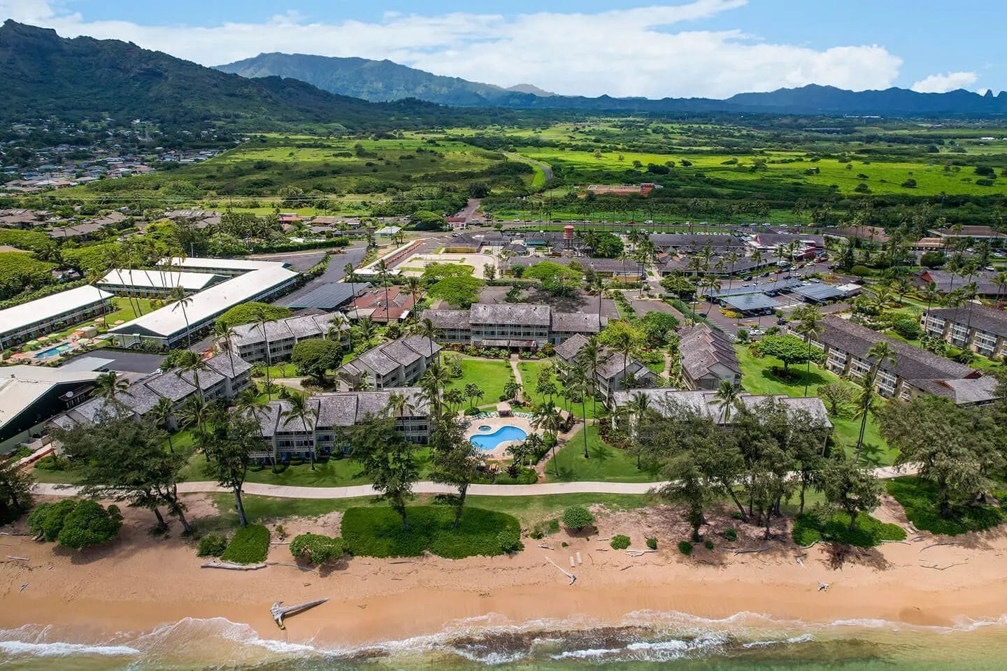 An aerial view of a resort with multiple buildings, a swimming pool, and a beach.