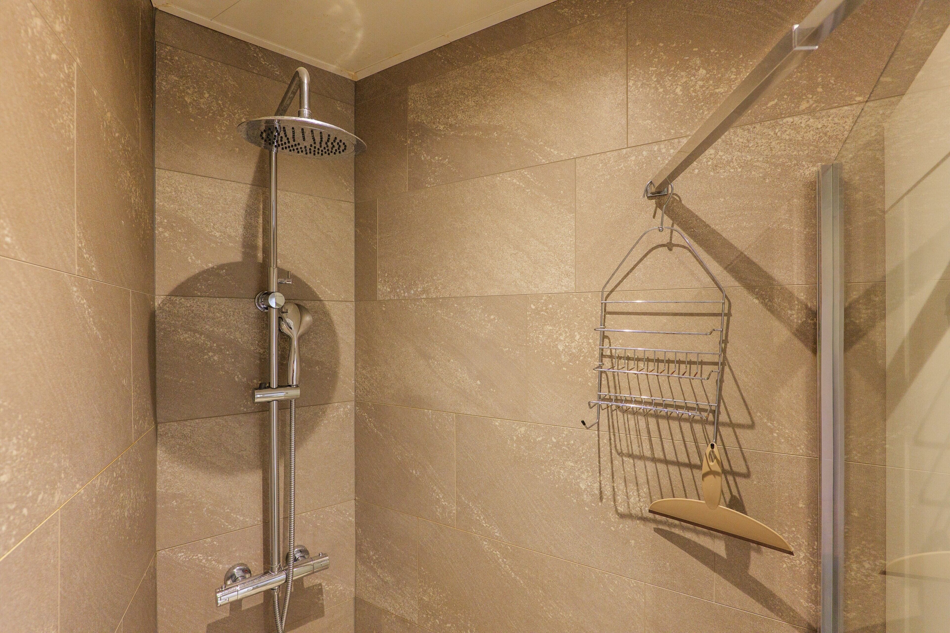 Eine Dusche mit Handbrause, einem Händetuchhalter an der Wand und einer Glasdusche.