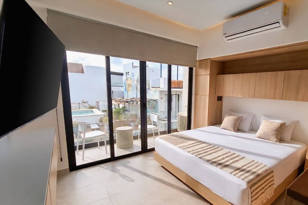 Een moderne slaapkamer met een groot bed, een schuifglasdeur naar een balkon en een airconditioning op de muur.