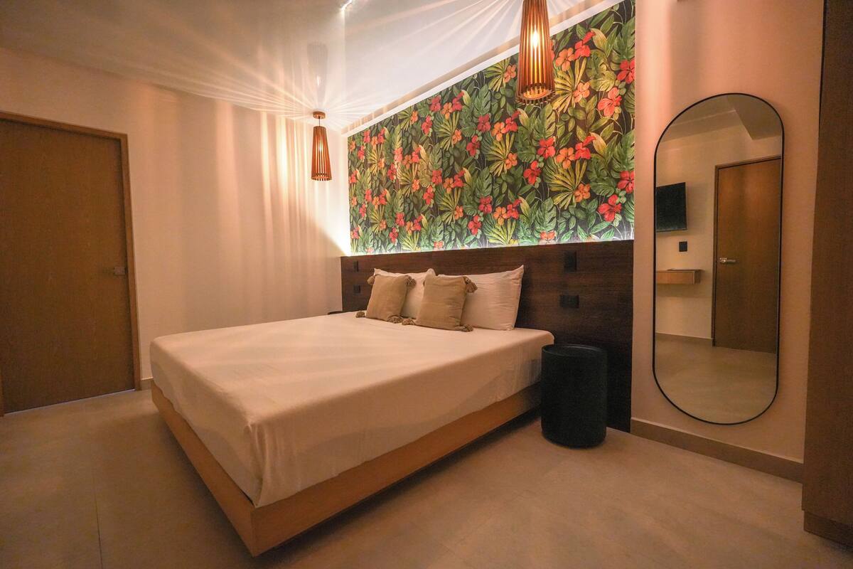 Een slaapkamer met een bed, een grote spiegel, een wand met bloemenmotief en een plafondlamp.