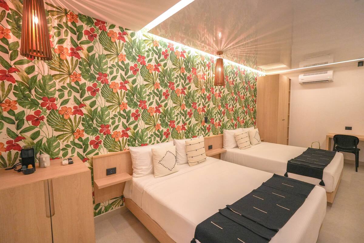 Een hotelkamer met twee bedden, een houten bureau, een klein tafeltje en een wand met een bloemenprint.