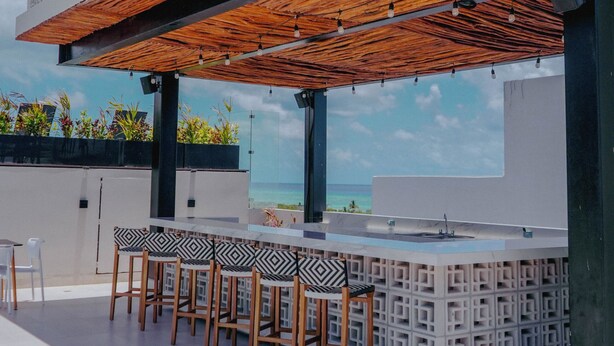 A rooftop bar with a geometric design, outdoor seating, and a view of the ocean. - Hotel Macondo Quinta Avenida by Ruha (Playa del Carmen)