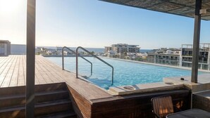 A rooftop pool with a wooden deck, metal pool ladder, and a view of the ocean and buildings. - Hotel Macondo Quinta Avenida by Ruha (Playa del Carmen)