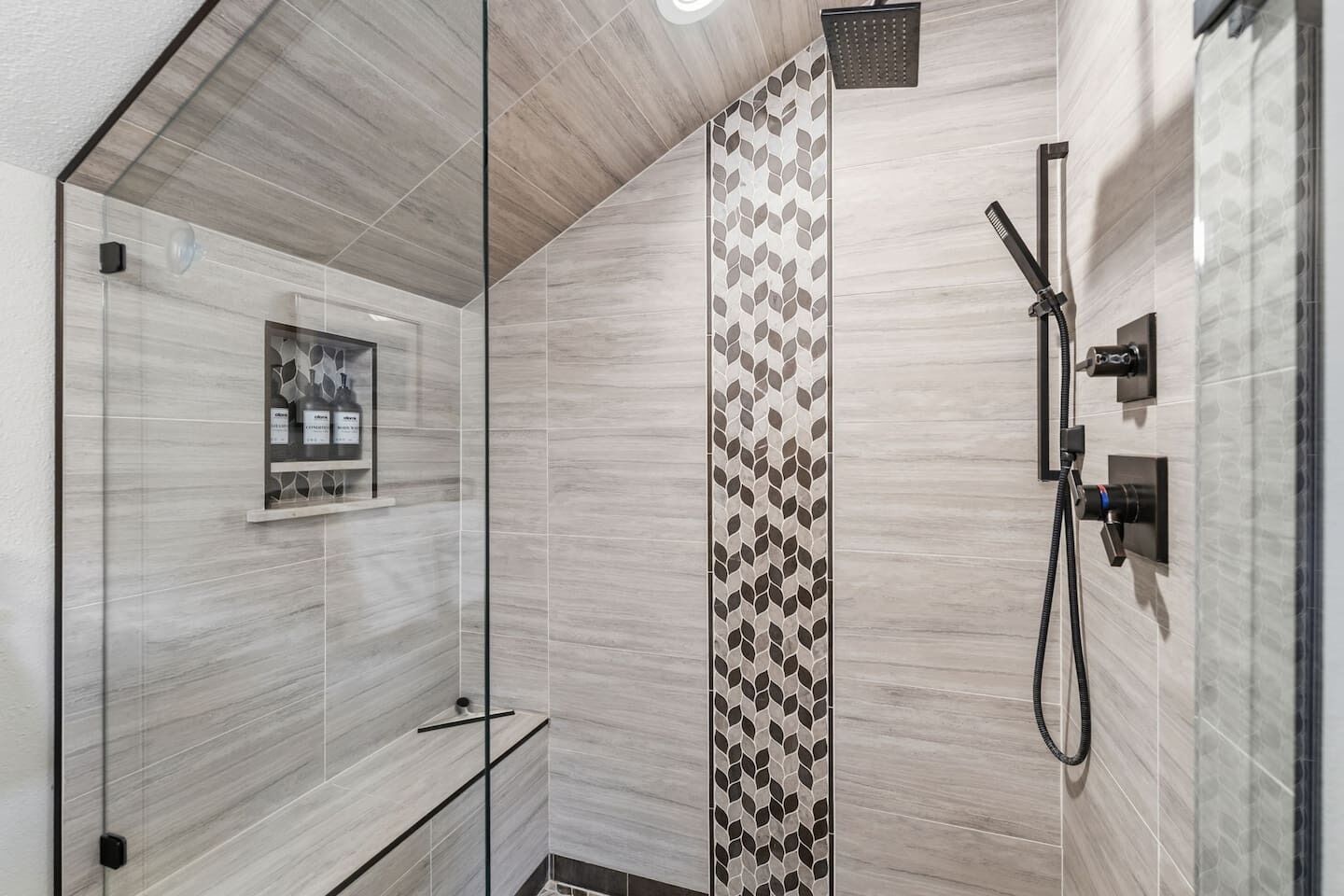 Un espacio de ducha moderno con puerta de vidrio, pared con diseño vertical y ducha de mano.