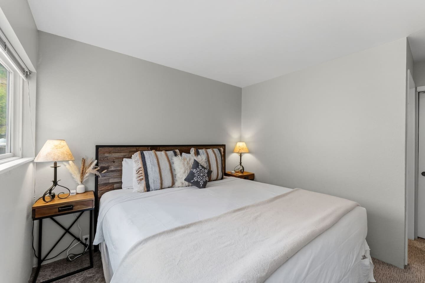 Quarto com cama grande, duas mesas de cabeceira com abajures, cabeceira de madeira e uma janela.