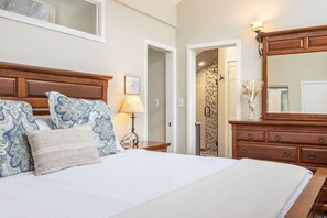 Un dormitorio con una cama grande, cabecera de madera, mesitas de noche, cómoda y espejo.