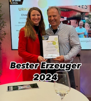 Two people holding a framed certificate with 'Bester Erzeuger 2024' text.
