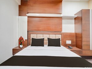 A hotel room with a bed, a nightstand, a vase with flowers, and a wardrobe. - Deluxehotel Navjivan (Himatnagar)