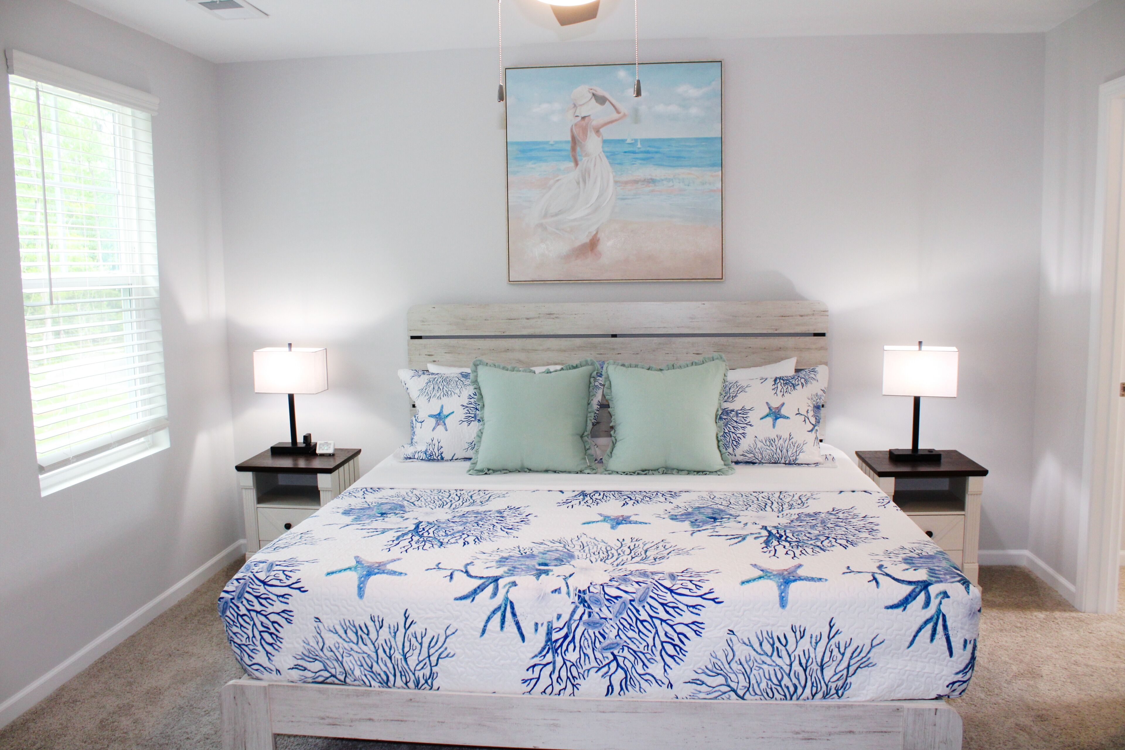 Une chambre à coucher avec un lit, deux tables de chevet, une commode, un tableau et une fenêtre.
