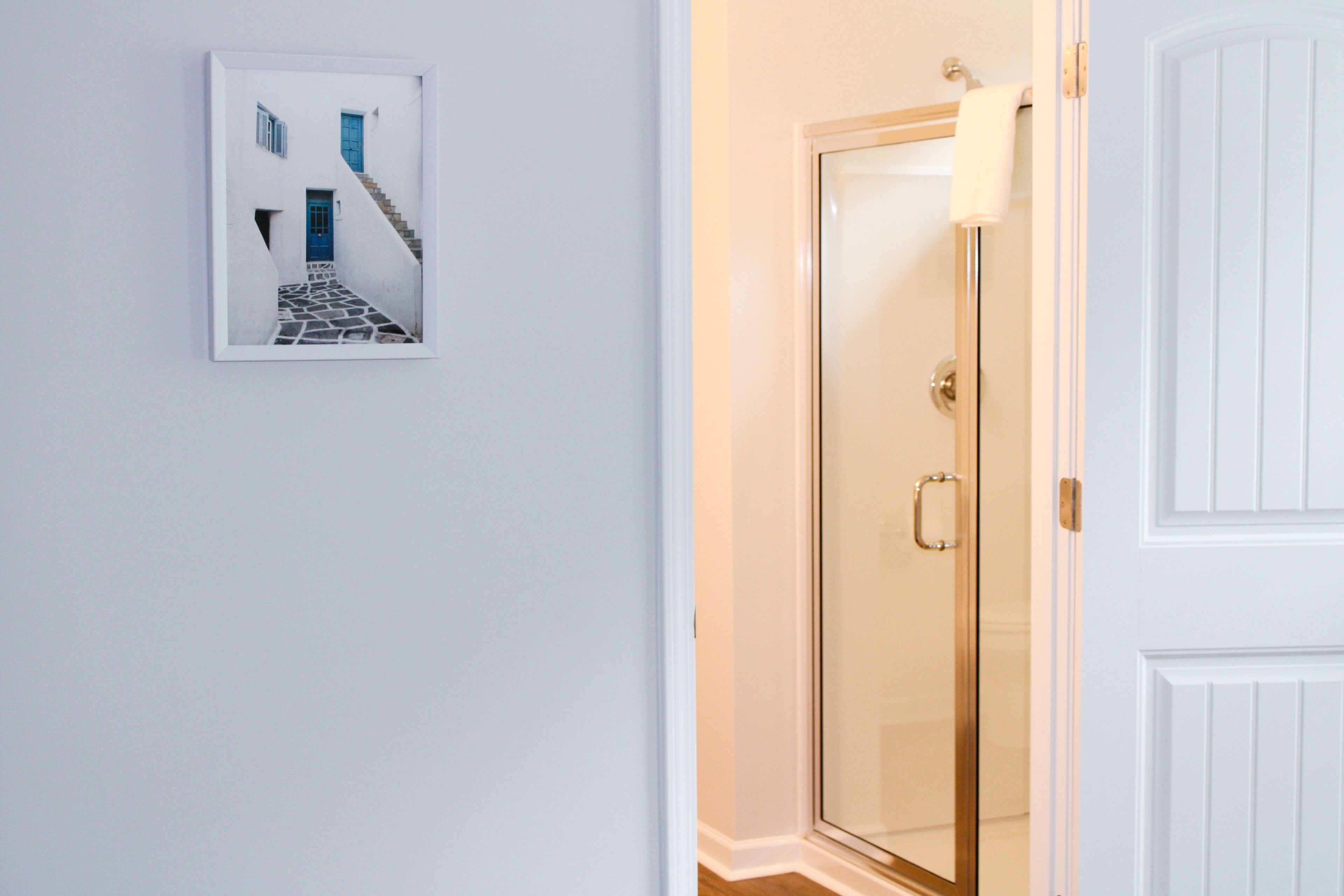 Une porte blanche avec un panneau de verre, un mur blanc et un tableau représentant une porte bleue et un escalier.
