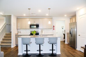 Una cocina moderna con una isla central, taburetes de bar, electrodomésticos de acero inoxidable y una escalera.