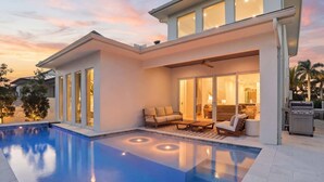 Et moderne hus med swimmingpool, en terrasse med udendørs møbler og en stor skydedør, der fører til et indendørs rum.