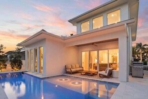 A modern house with a swimming pool, a patio with outdoor furniture, and a large sliding glass door leading to an interior space. - New Luxury Retreat - Resort Pool - Walk to Beach (Naples)