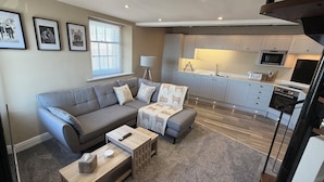 Un salón moderno con un sofá gris, una mesa de centro y una cocina al fondo.