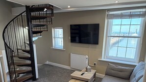 Una sala de estar con un sofá gris, una mesa de centro, un televisor, una chimenea y una escalera en espiral.
