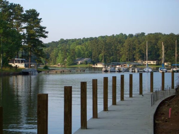 Eine Uferpromenade mit Holzpfählen, ruhigem Wasser und einer bewaldeten Hügelkette im Hintergrund.