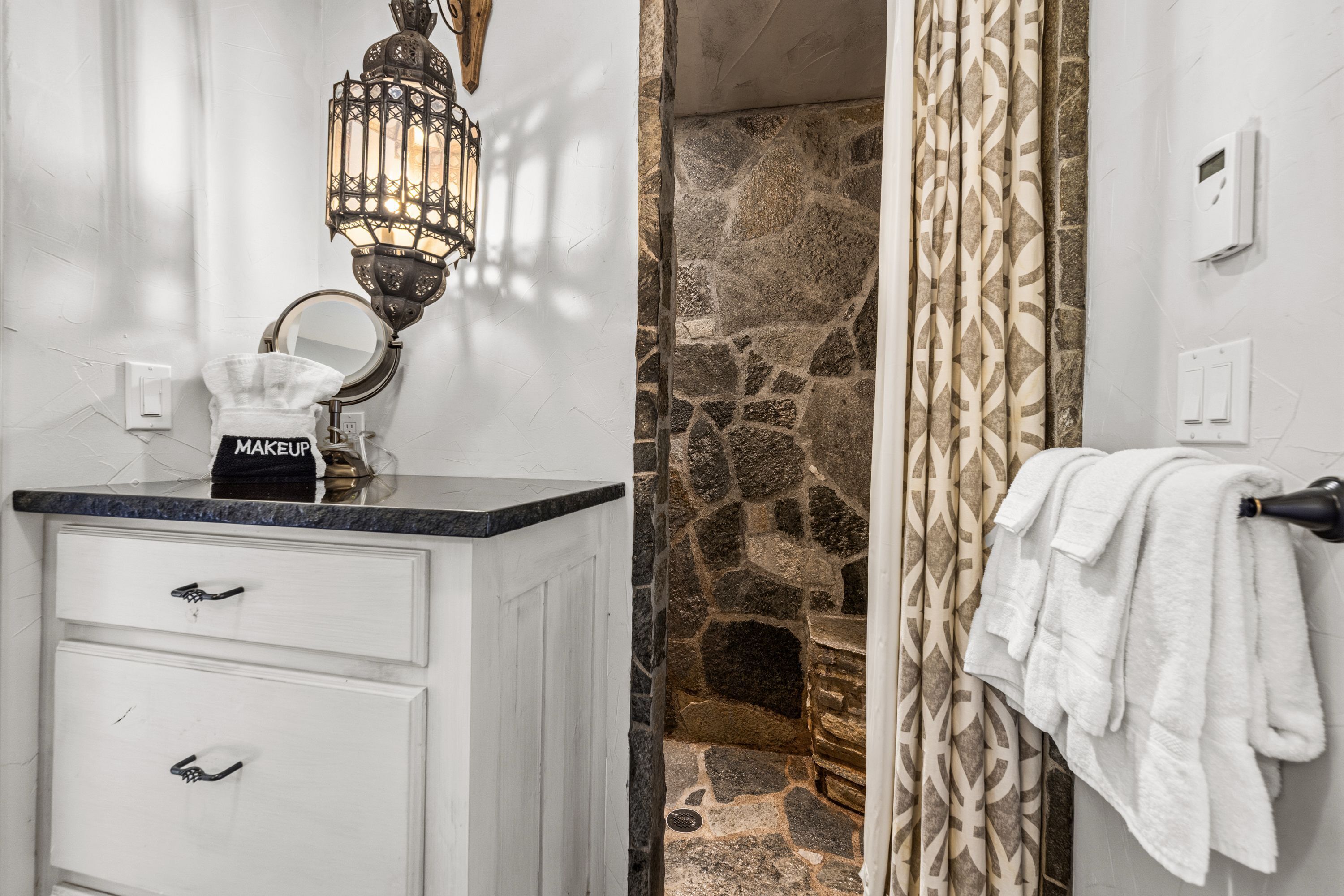 A bathroom with a stone wall, a mirror, a towel rack, and a decorative lantern.