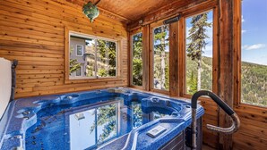 Eine Holzhütte mit Whirlpool, großen Fenstern und Blick auf den Wald.