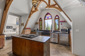 A kitchen with a central island, wooden beams, and stained glass windows.