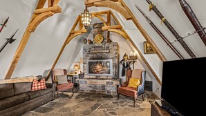 Ein Loft-Zimmer mit Kamin aus Stein, Holzbalken, einem Fernseher und einer gemütlichen Sitzecke.