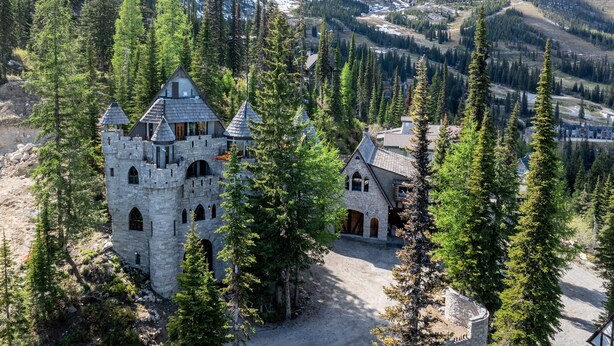 Ein burgartiges Steinhaus, umgeben von dichtem Wald und schneebedeckten Bergen im Hintergrund.