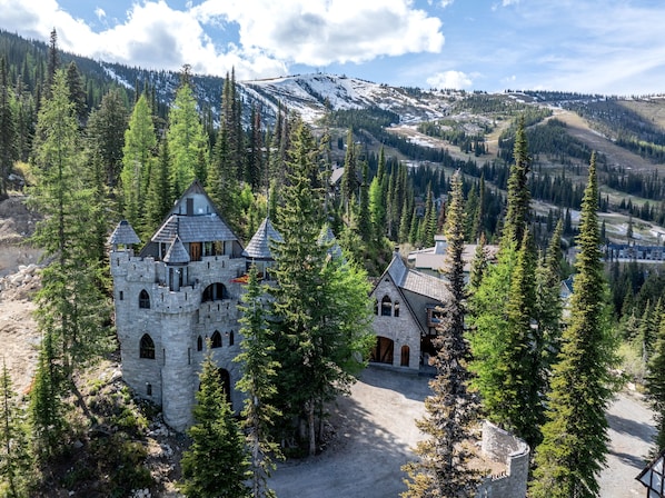 A stone castle-like structure surrounded by dense forest and snow-capped mountains.