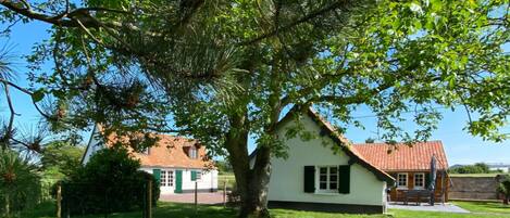 A white house with a red roof, surrounded by a well-maintained lawn and a large tree.