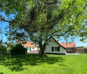 A white house with a red roof, surrounded by a well-maintained lawn and a large tree.