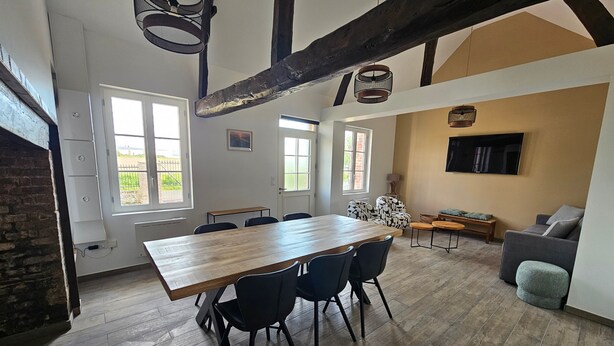 Un grand espace dédié à la salle à manger, avec une longue table en bois et des chaises, un canapé et un téléviseur fixé au mur.