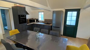 Et moderne køkken med en central ø, indbyggede apparater og et spiseområde med et stort bord og stole.