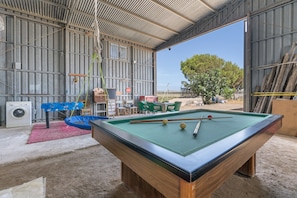 Une table de billard dans une pièce spacieuse, dotée d’une grande fenêtre, d’un lave-linge et d’un espace salon extérieur.