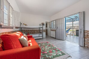 Une pièce avec un lit superposé, un canapé rouge, un tapis à motifs et une vue sur la plage par une porte ouverte.
