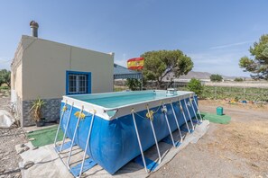 A swimming pool with a blue and white exterior, a small building with a blue window, and a flag in the background.