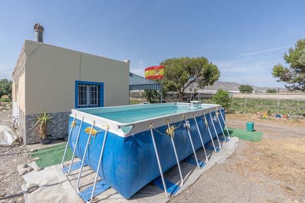 Une piscine aux couleurs bleu et blanc, un petit bâtiment avec une fenêtre bleue et un drapeau en arrière-plan.