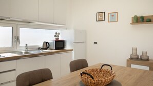 A modern kitchen with white cabinets, a microwave, and a kettle on the counter. There is a dining table with a woven basket and chairs. - La Dimora Molara by Wonderful Italy (Olbia)