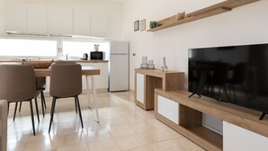 A modern kitchen with white cabinets, a dining area with two chairs, a TV on a wooden stand, and a shelf with decorative items. - La Dimora Molara by Wonderful Italy (Olbia)