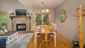 Comedor con chimenea de piedra, mesa de madera, sillas y un amplio ventanal con vistas a la vegetación.